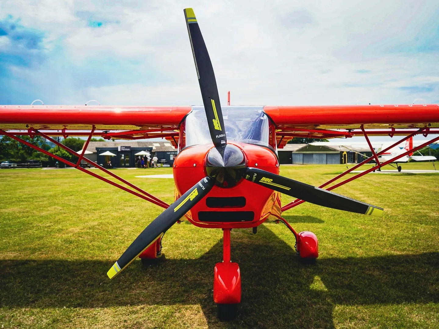 A red propeller plane is parked on a grassy field with a clear sky above.