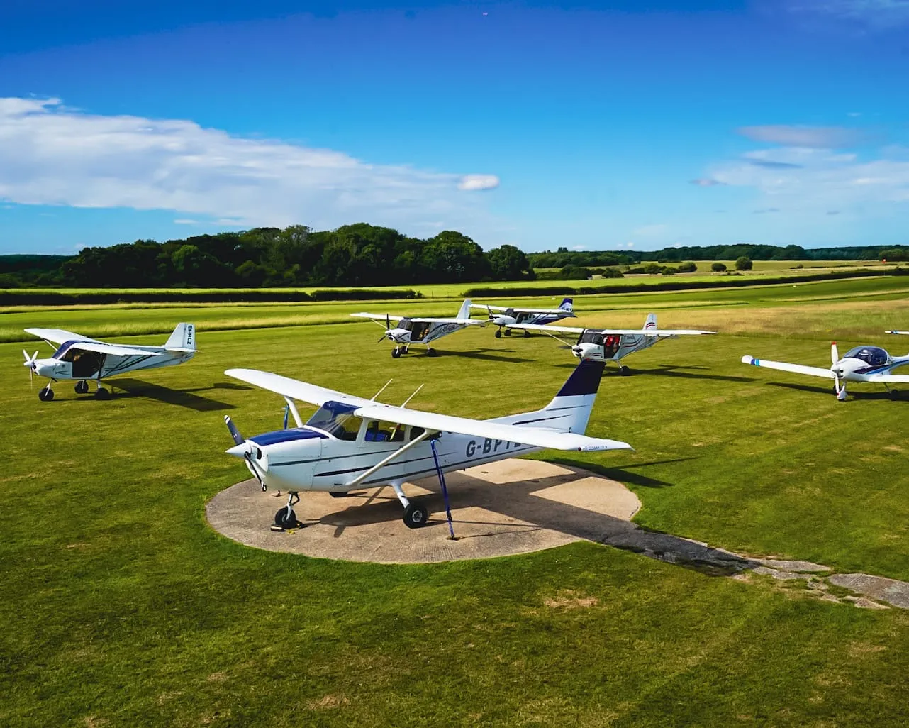 Several small airplanes parked on a grassy field under a clear blue sky.