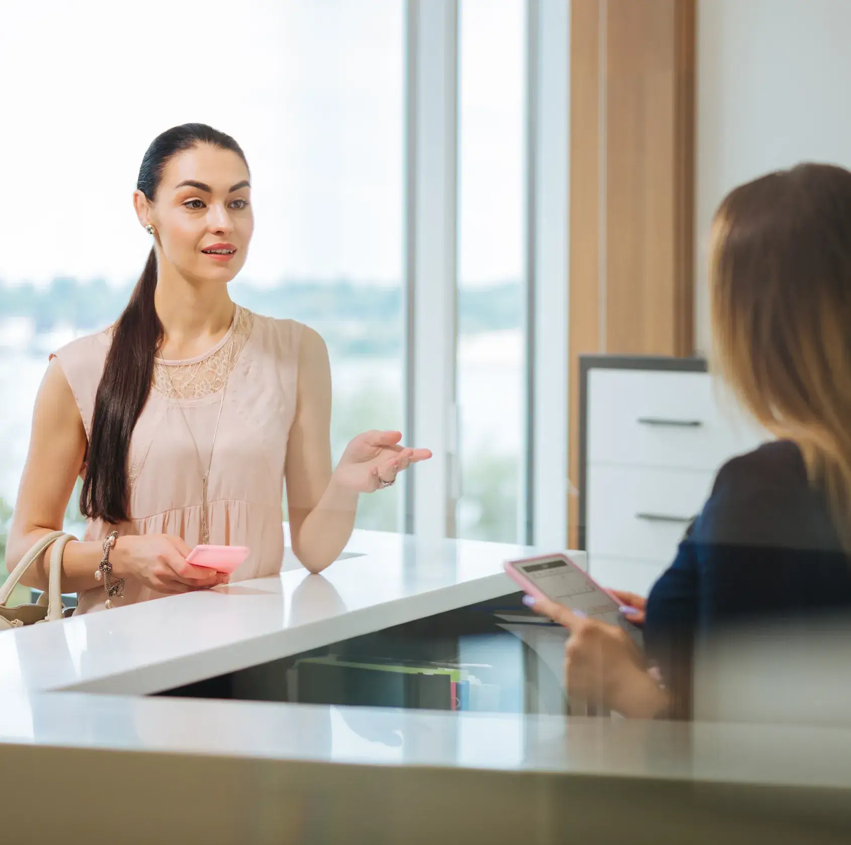 A woman talking to another woman at a desk.