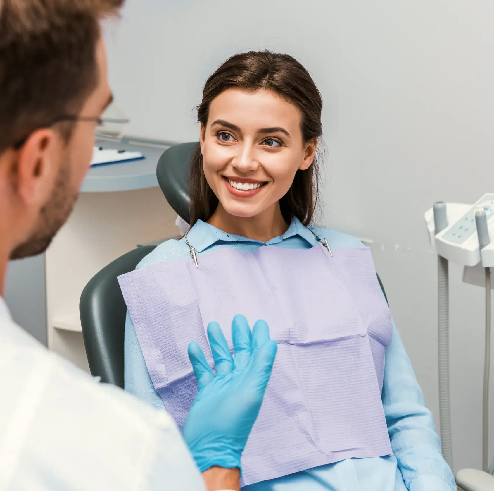 A woman sitting in a dentist chair with a blue glove.