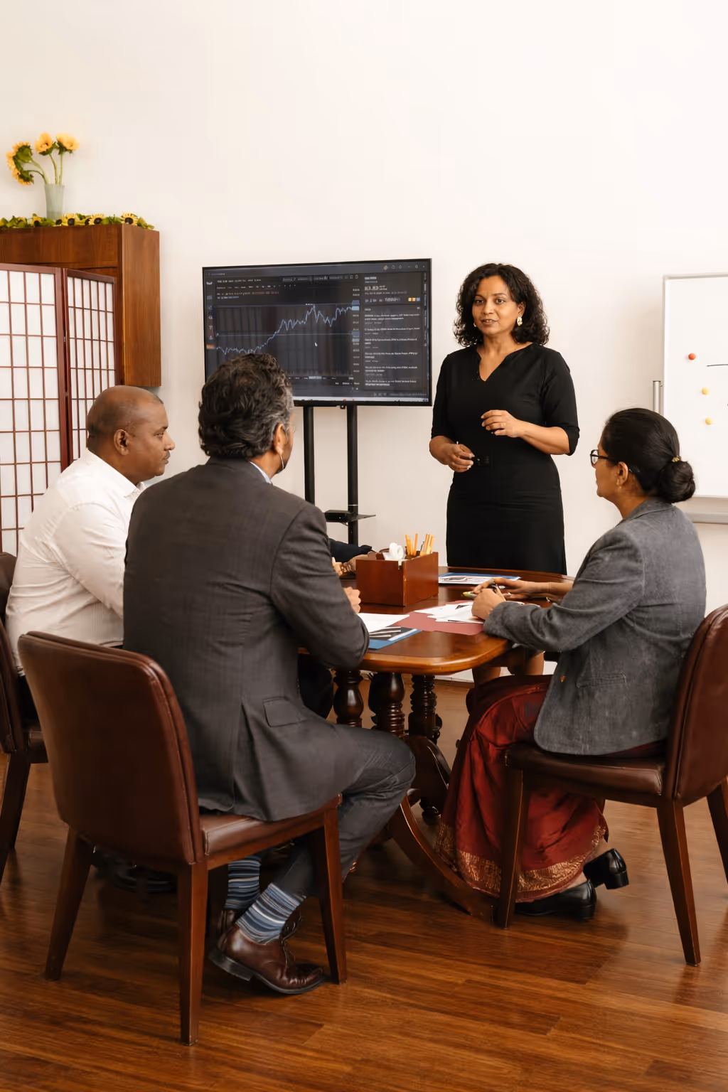 A woman presenting data on a screen to three colleagues seated around a meeting table