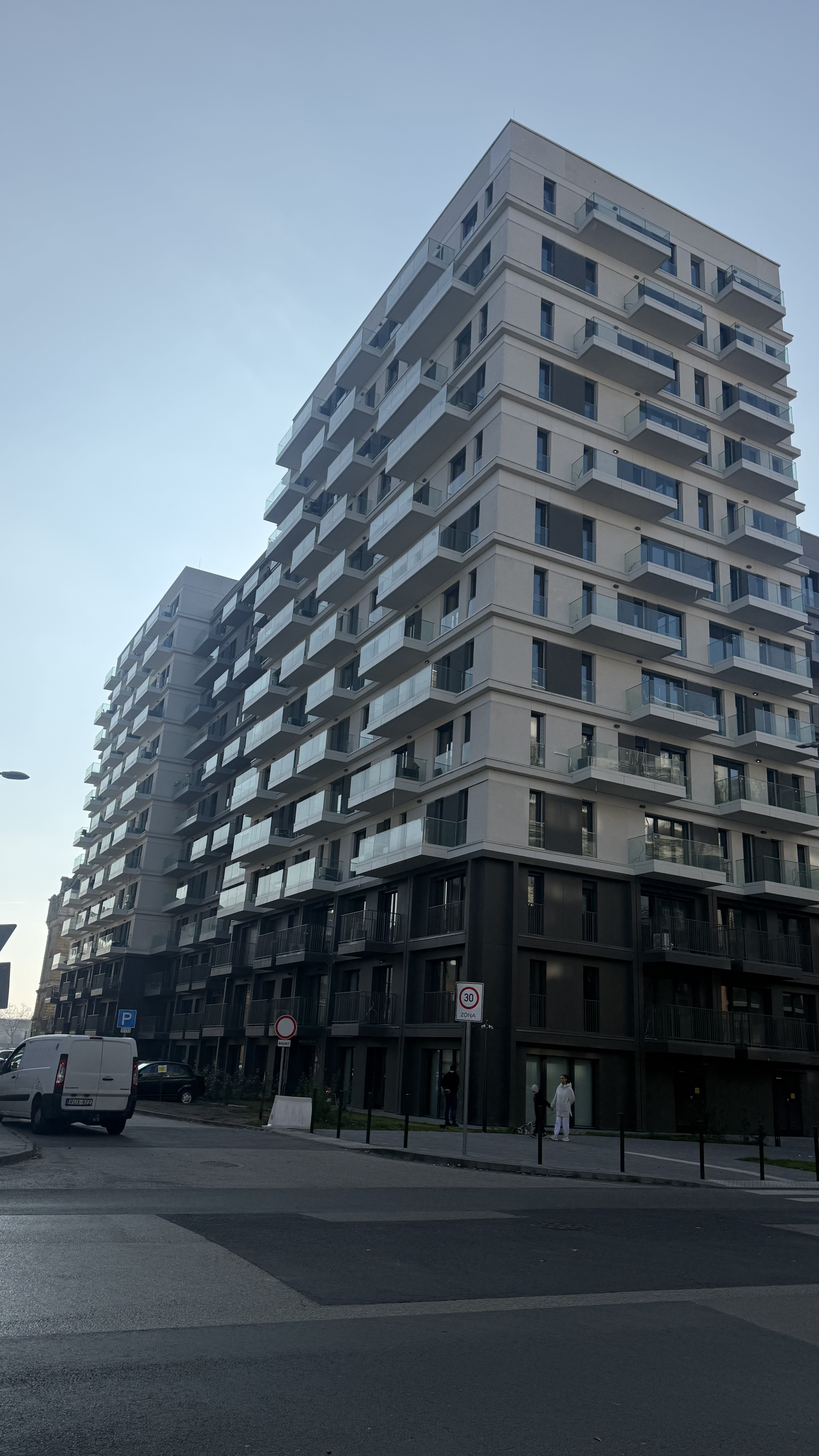 Modern multi-story apartment building with glass balconies under a clear sky.