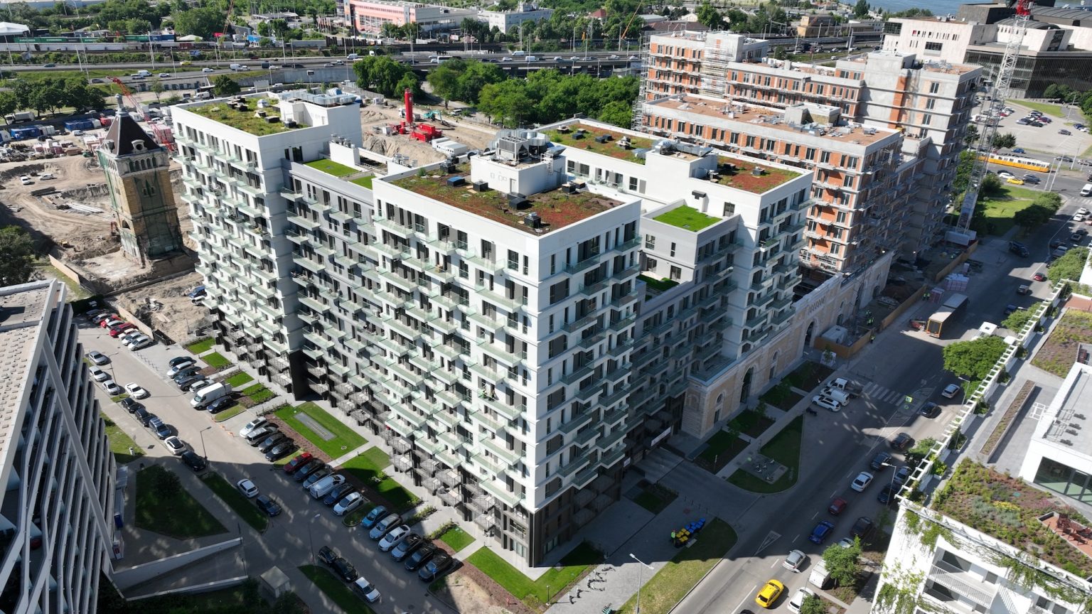 Aerial view of modern residential buildings with green rooftops and surrounding streets filled with parked cars.