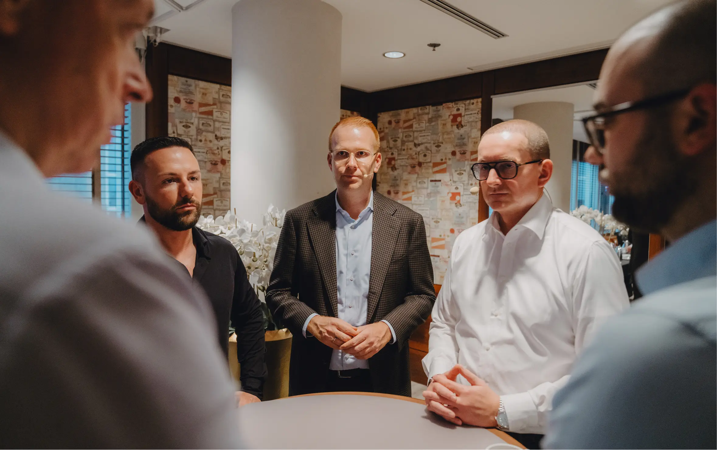 Fünf Geschäftsmänner stehen um einen runden Tisch in einem Büro und führen eine ernste Diskussion.