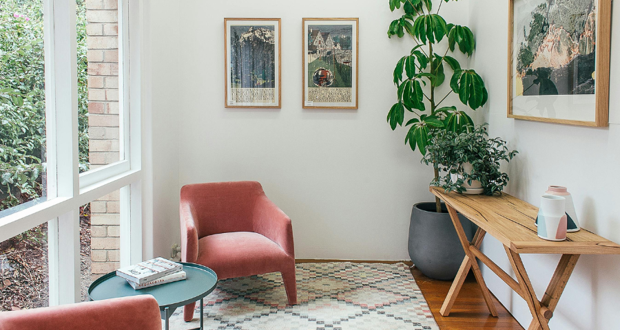 Bright modern living room with wooden dining table, gray chairs, beige sofa, and dark cabinets with built-in oven.