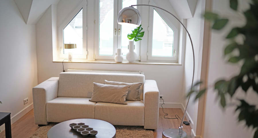 Minimalist bedroom with white bed, wooden slat room divider, small wooden table with black chairs, and a wall-mounted TV.