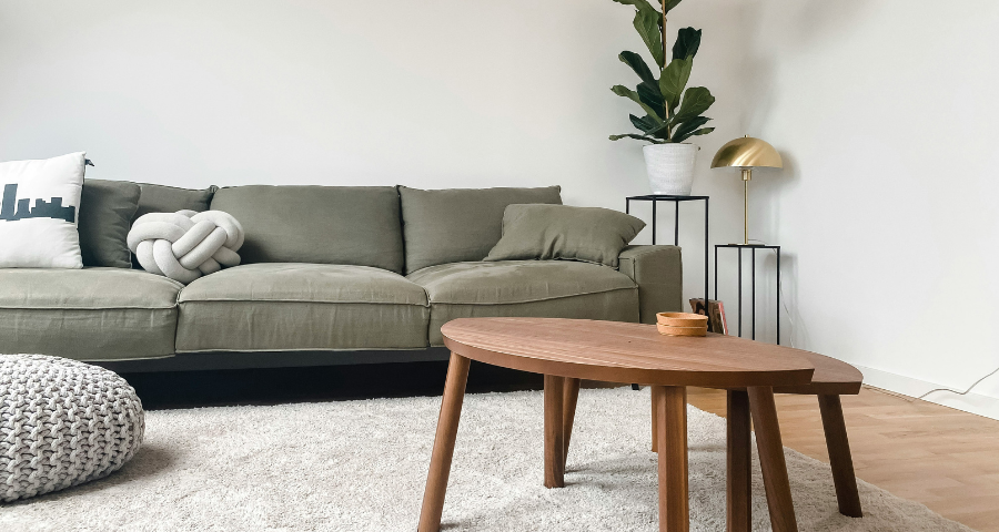 Cozy living room with tan sofa, rattan chair, wooden tables, a TV displaying Netflix, and a large window letting in natural light.