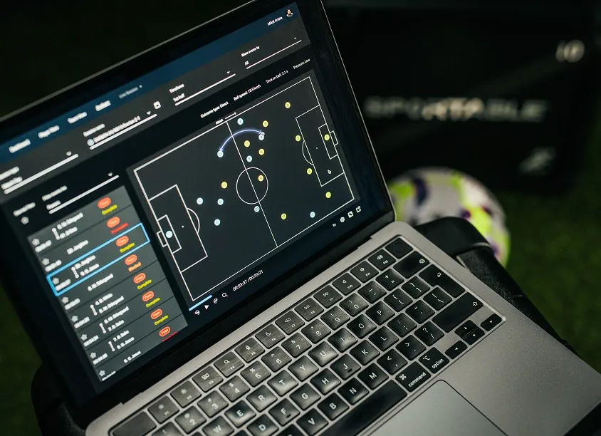 Laptop screen displaying a soccer tactics board with player positions and movement arrows.