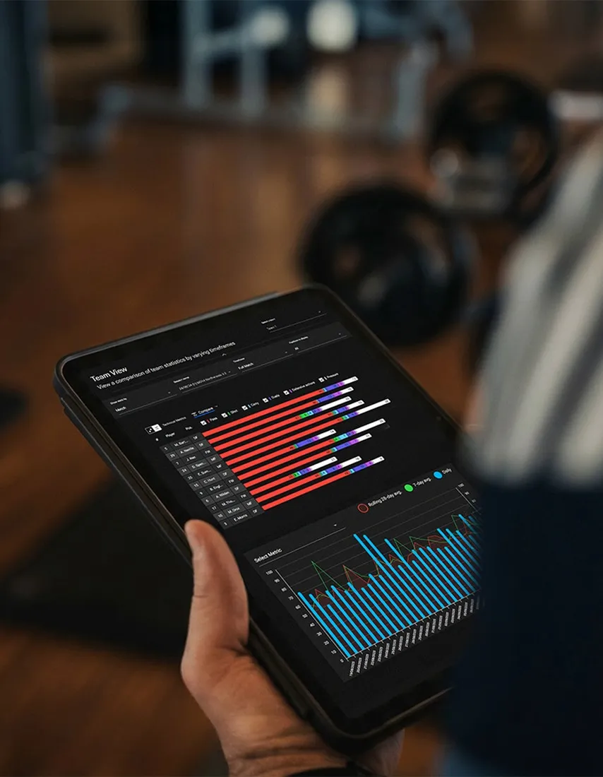 Hand holding a tablet displaying team statistics and performance bar and line charts in a gym setting.