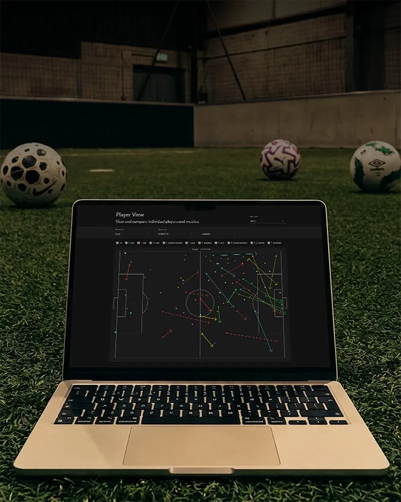 Laptop on a soccer field displaying a tactical soccer analysis with colored player movement lines on the screen.