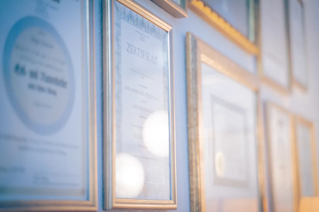 Wall displaying multiple framed certificates with gold trim in soft focus.