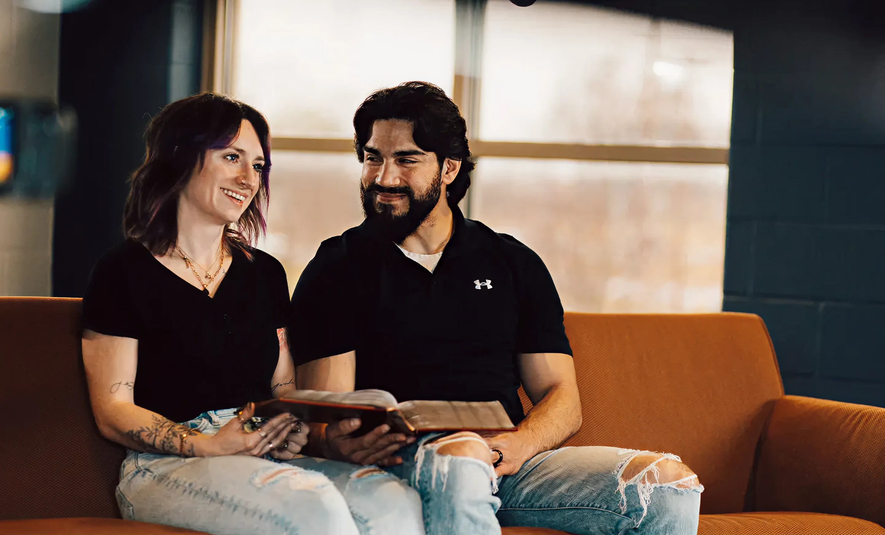 Smiling man and woman sitting on a couch reading a book together.