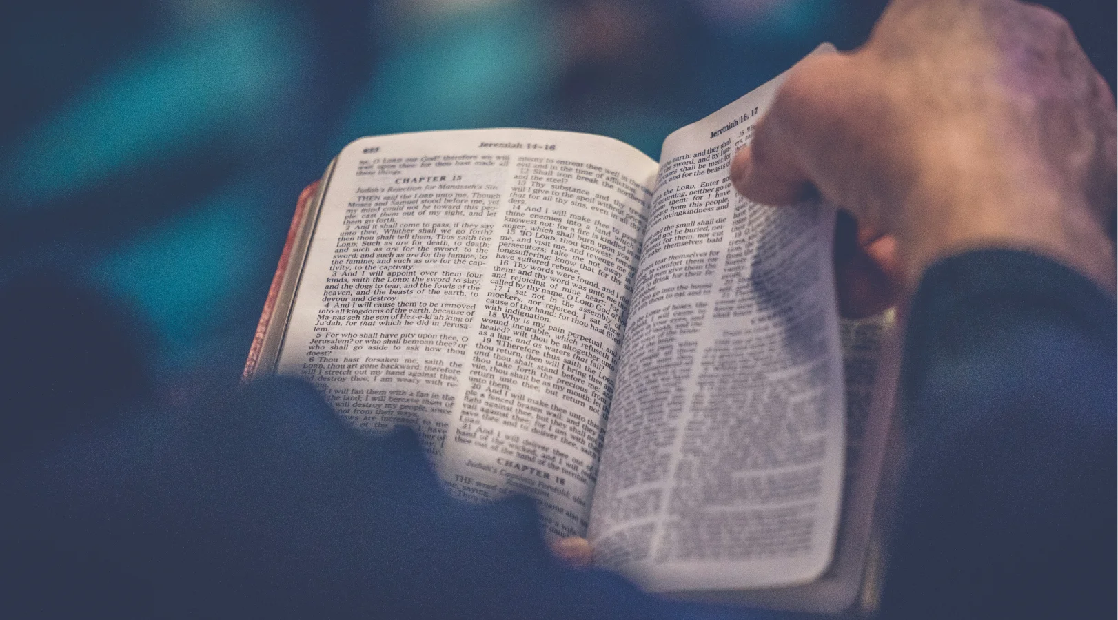 Close-up of hands holding and reading an open Bible showing the book of Jeremiah.