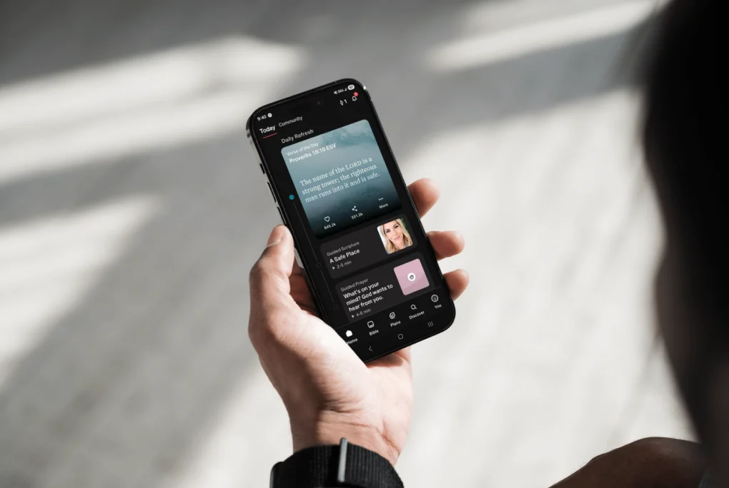 Person holding smartphone displaying a Christian podcast app with daily scripture and guided prayers.