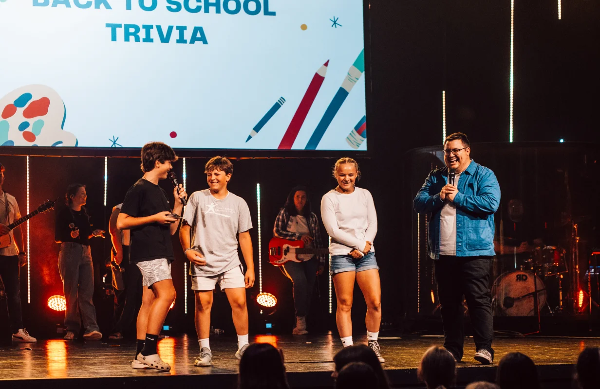 Group of young people and a man with microphones on stage during a back-to-school trivia event.