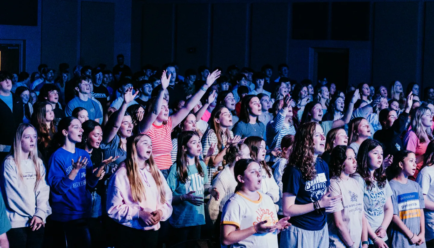 Large group of young people worshipping with eyes closed and hands raised during a youth service.