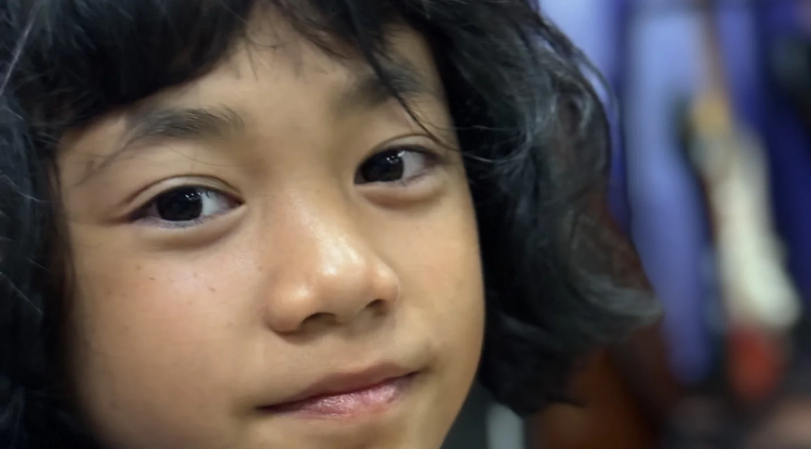 Close-up of a young child with dark hair looking directly at the camera with a slight smile.