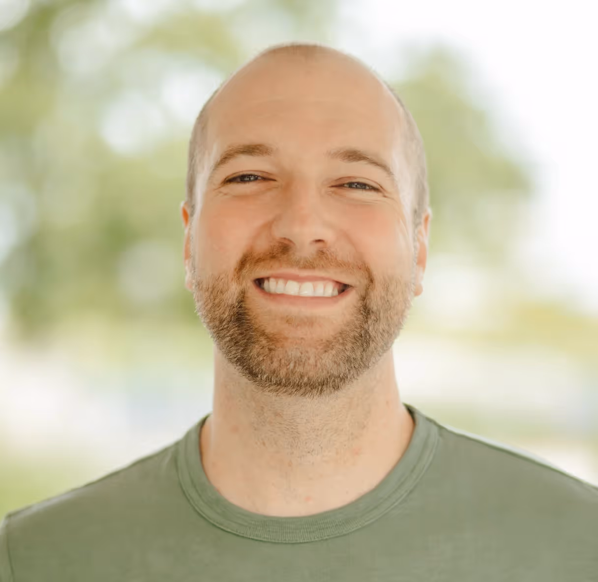 Smiling man with a trimmed beard outdoors wearing a green t-shirt.