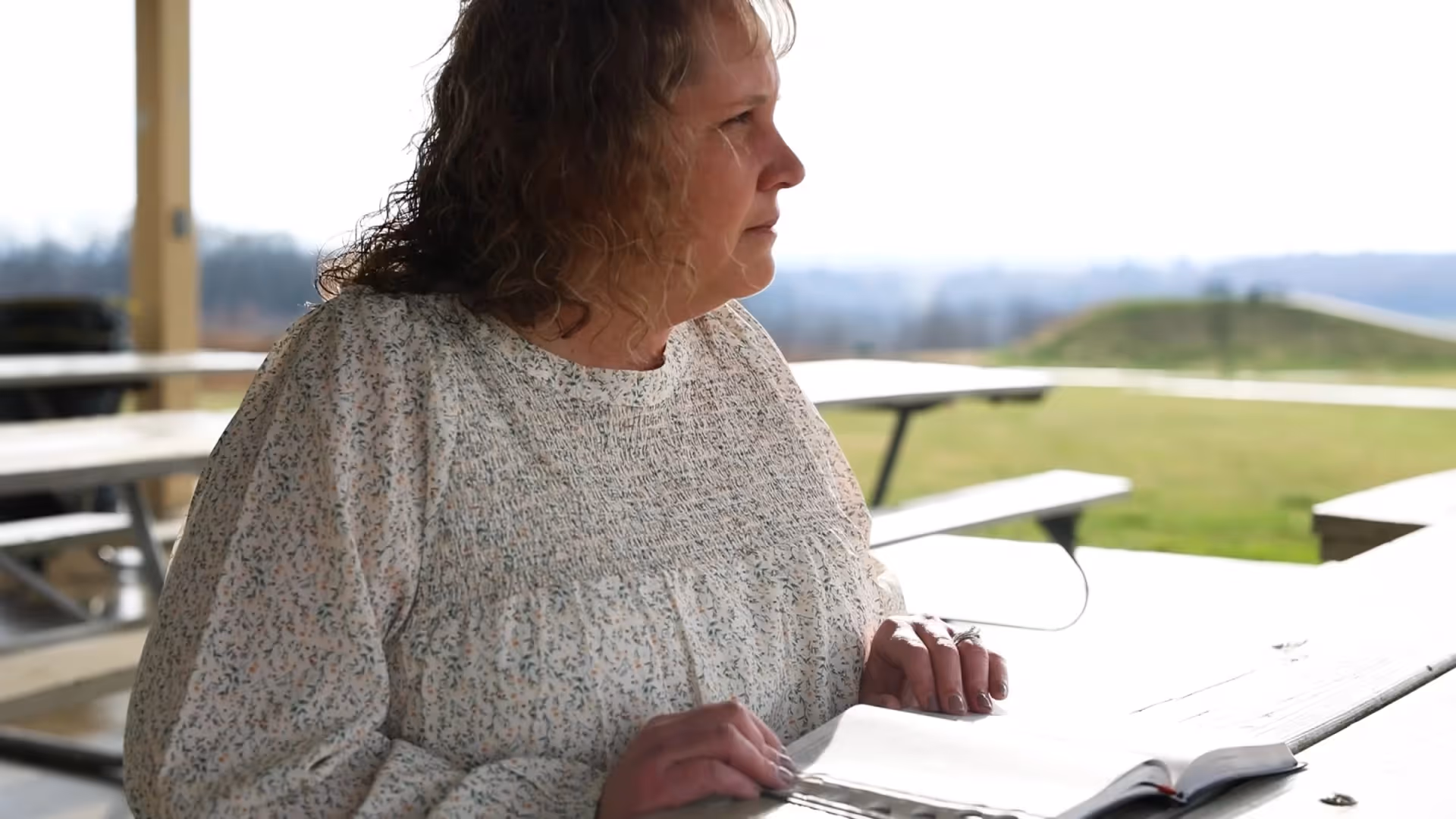 Woman sitting outdoors at a picnic table reading papers in natural light.