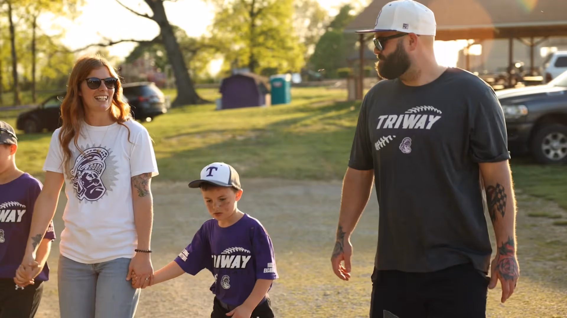 Family walking outdoors in sunlight with two children wearing matching shirts.