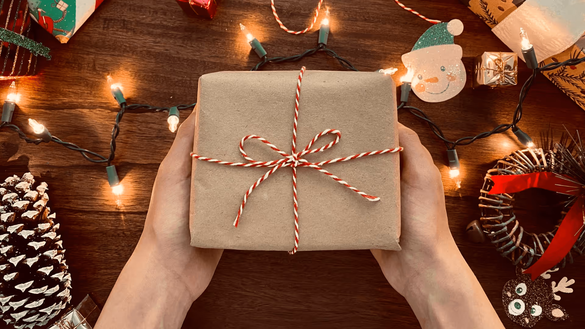 Hands holding a Christmas present in wrapped in brown kraft paper with a red and white ribbon