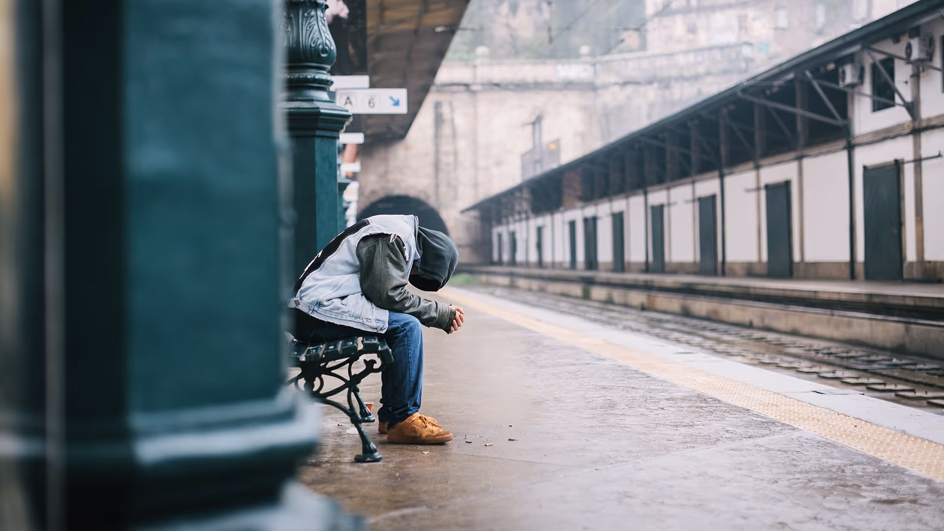 person sitting hunched over on bench at train station
