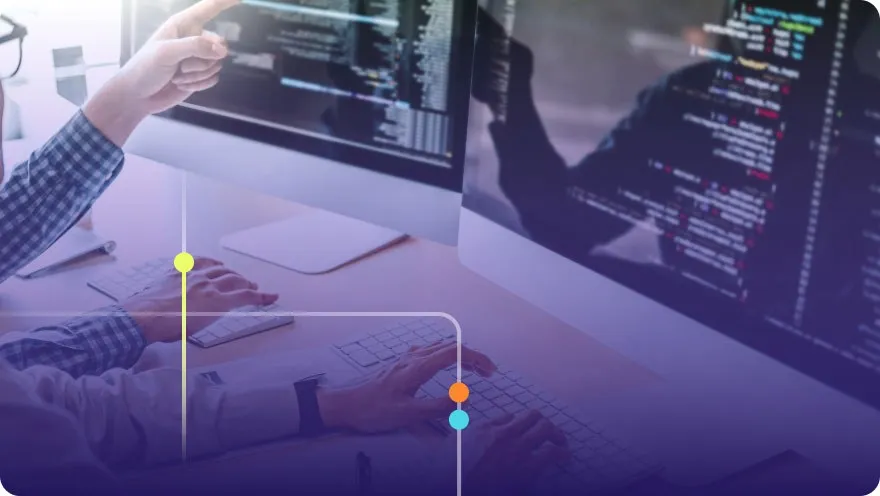 Two developers collaborating at a desk with multiple monitors showing code