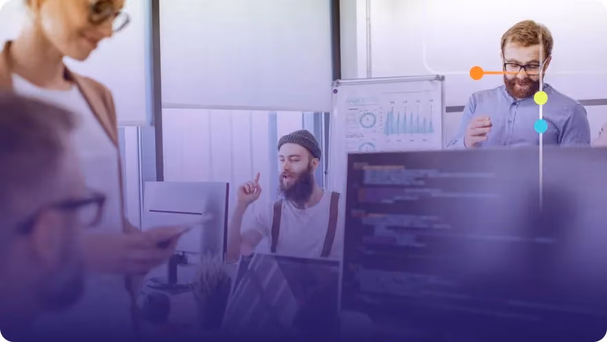 Team discussing around monitors and a whiteboard with analytics charts in a tech office