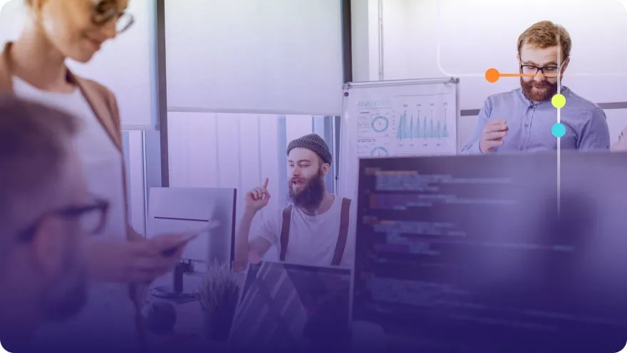 Team discussing around monitors and a whiteboard with analytics charts in a tech office