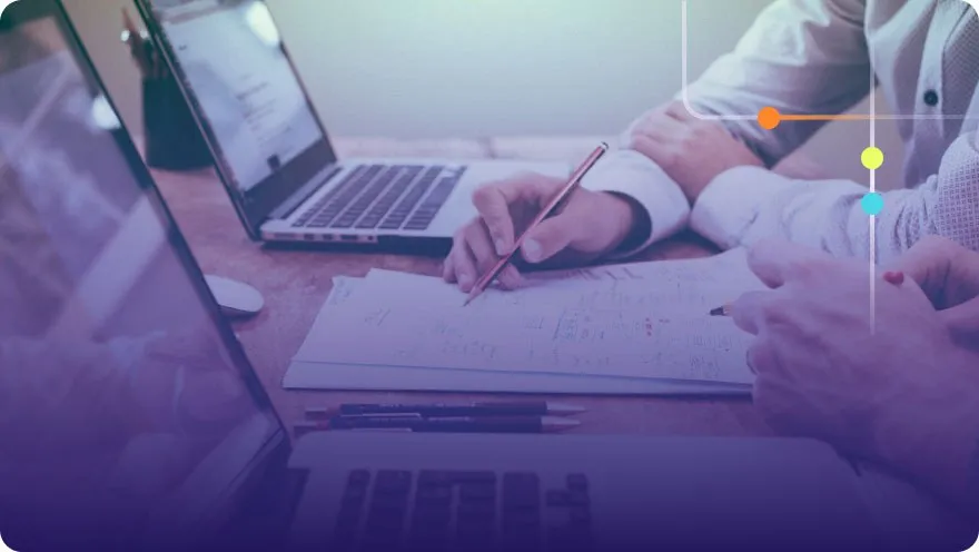 Team members writing notes on paper next to laptops during a collaborative work session