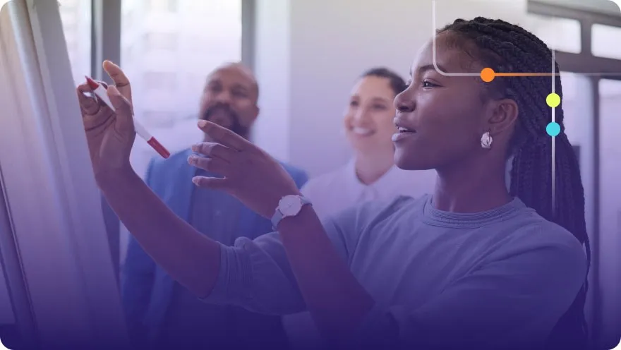 Woman writing on a whiteboard during a team presentation with colleagues watching