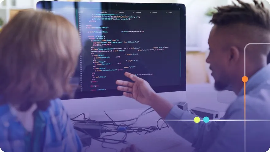 Two developers pair programming while reviewing HTML code on a large monitor