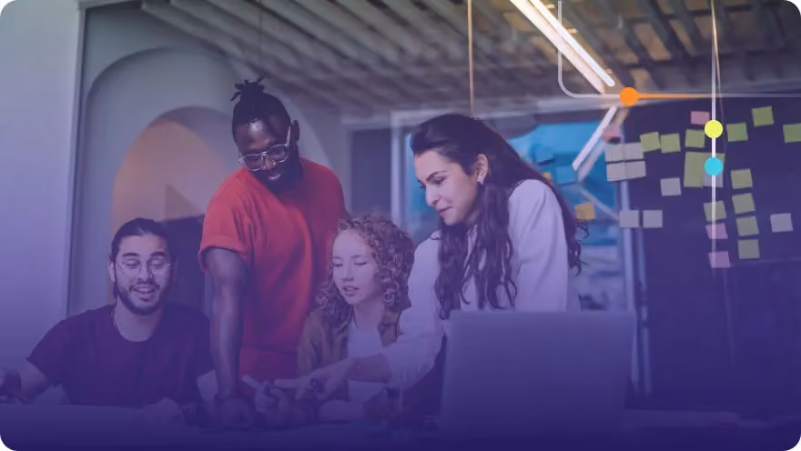Diverse team of four collaborating around a laptop with sticky notes on a glass wall behind them