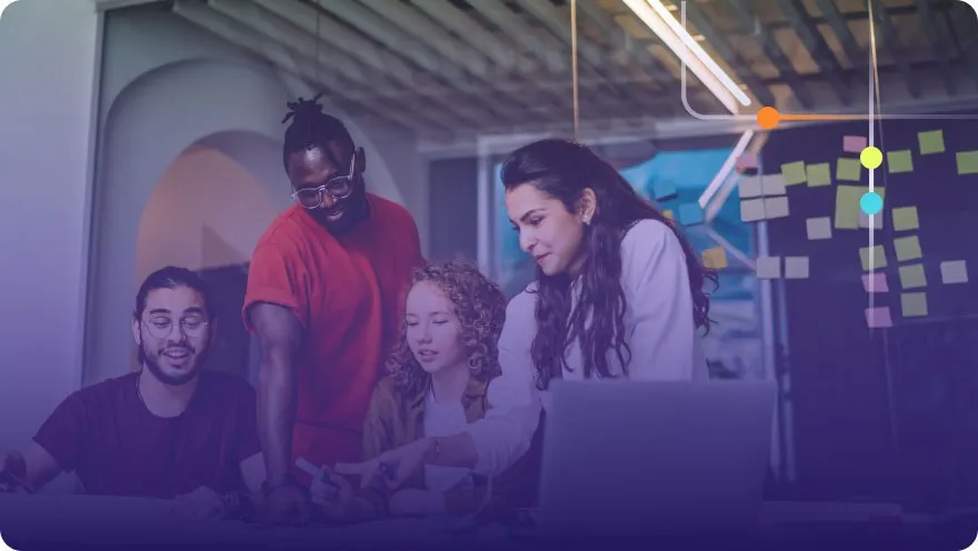Diverse team of four collaborating around a laptop with sticky notes on a glass wall behind them