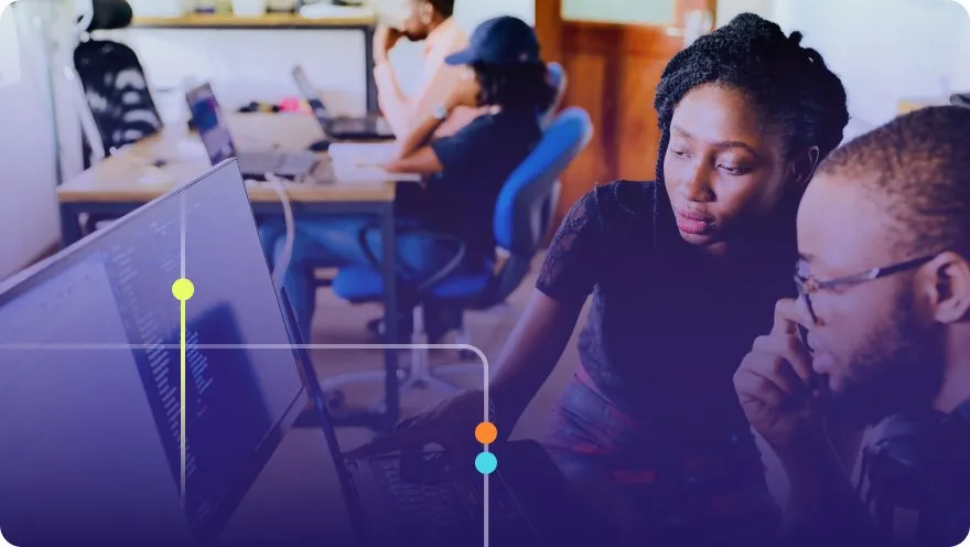 Two developers reviewing code together on monitors in a collaborative office environment