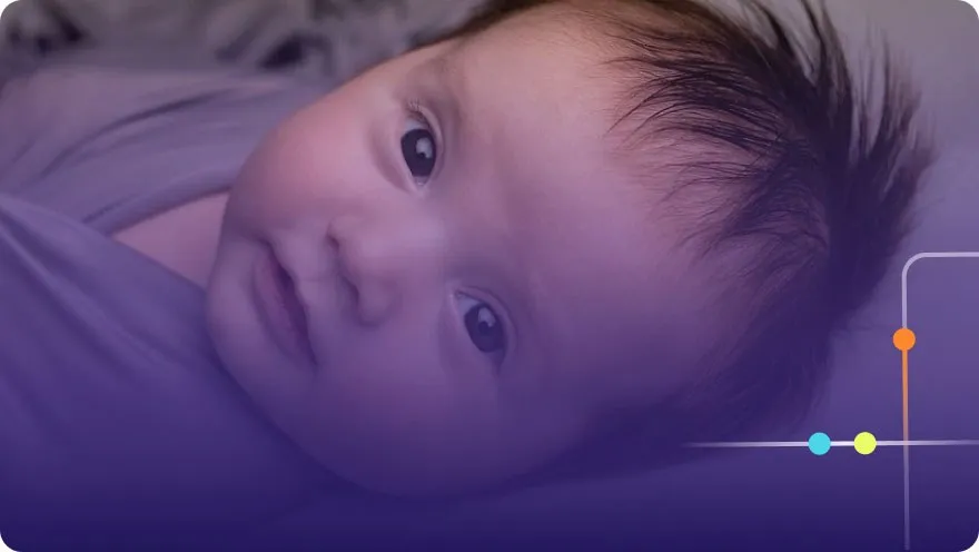 Newborn baby with dark hair lying on a blanket looking at the camera