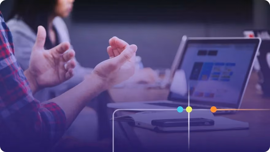 Person gesturing while discussing near a laptop showing colorful app designs, purple overlay