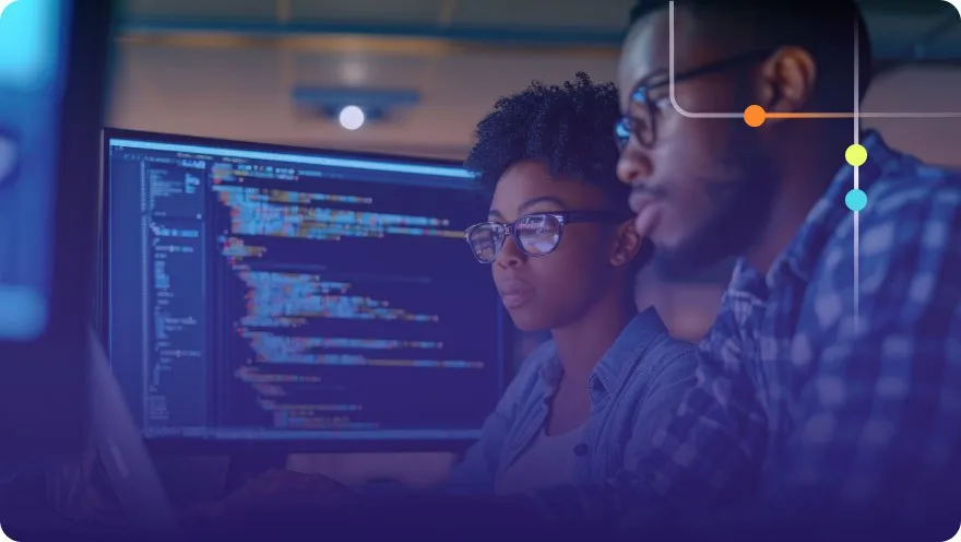 Two developers reviewing code together on a monitor with lines of code reflected in their glasses