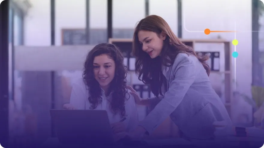 Two women smiling while looking at a laptop screen together in an office with a purple overlay