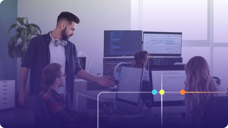 Software development team collaborating around multiple monitors with code on screen in a modern office