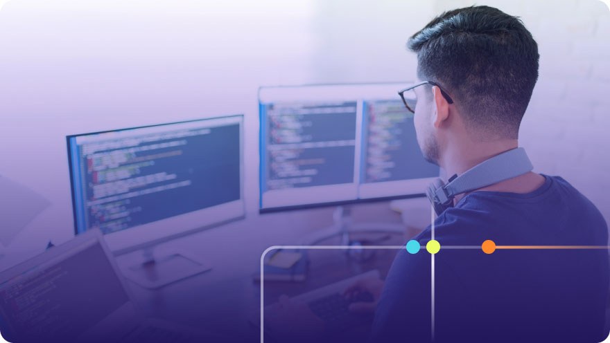 Developer with glasses working at a multi-monitor setup displaying code with purple overlay