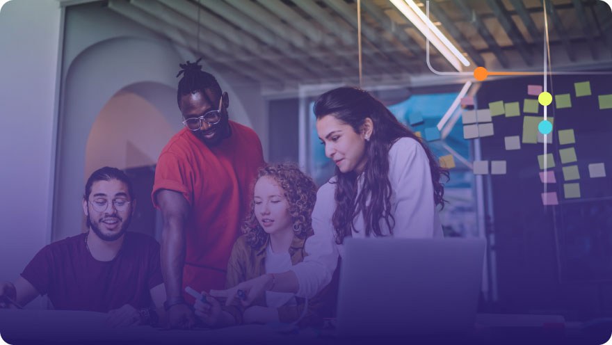 Diverse team of four collaborating around a laptop with sticky notes on a glass wall behind them
