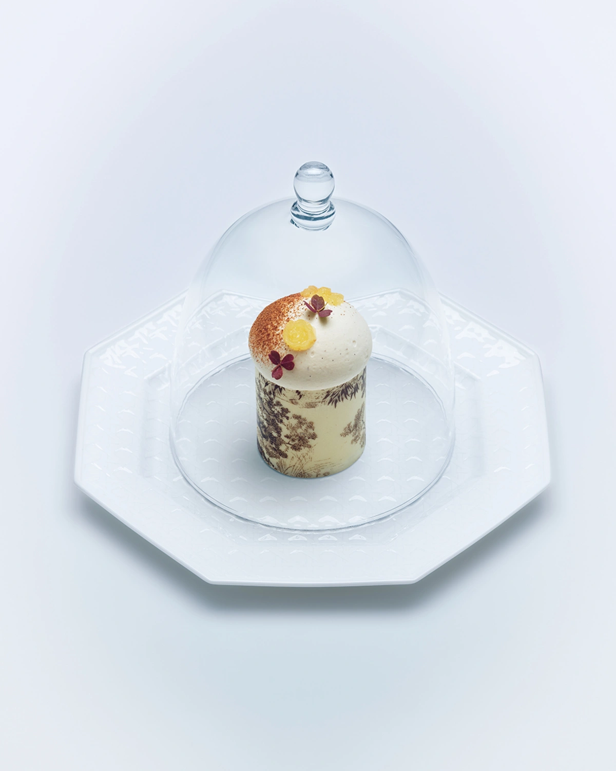 Pâtisserie fine et aérienne présentée avec élégance sous une cloche de verre protectrice.