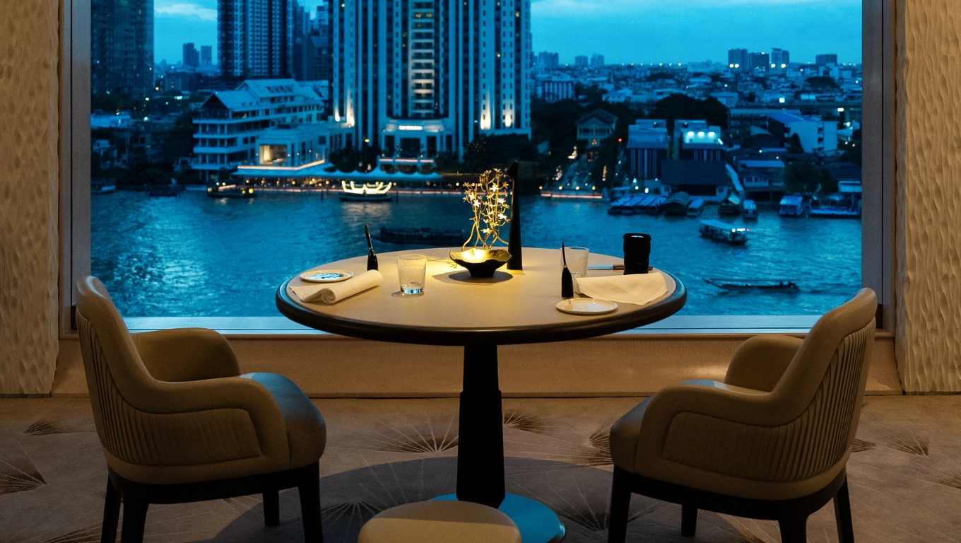 Table dressée pour deux devant une grande baie vitrée offrant une vue panoramique sur une ville au crépuscule.