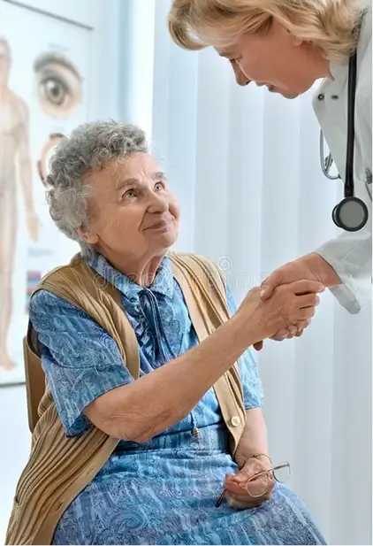 Smiling elderly woman sitting and holding hands with a female doctor in a medical office.