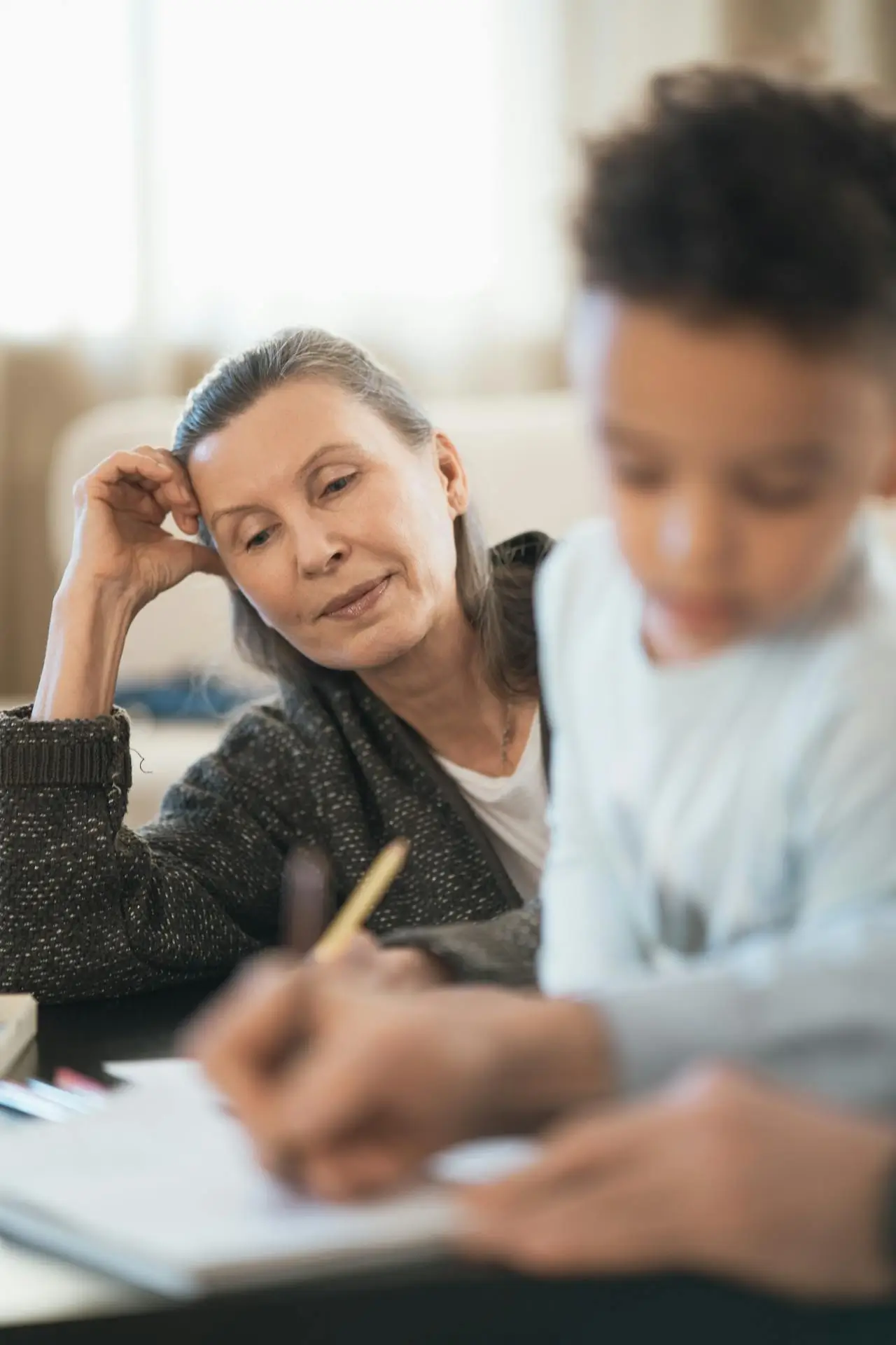 Older woman watching attentively as a child writes in a notebook.