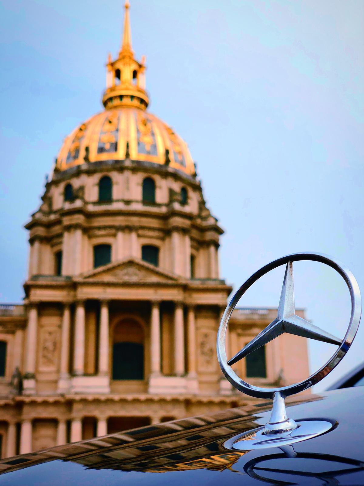 Emblema Mercedes-Benz em capô de carro com cúpula dourada do edifício Les Invalides ao fundo.
