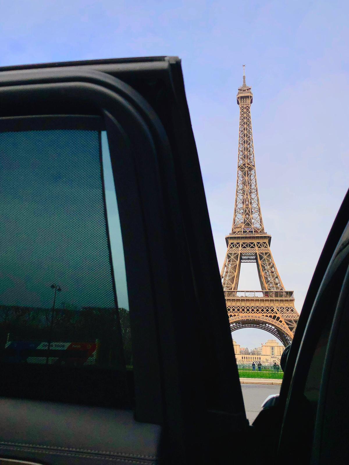 Tour Eiffel vue depuis une voiture avec la portière ouverte sur un ciel clair.