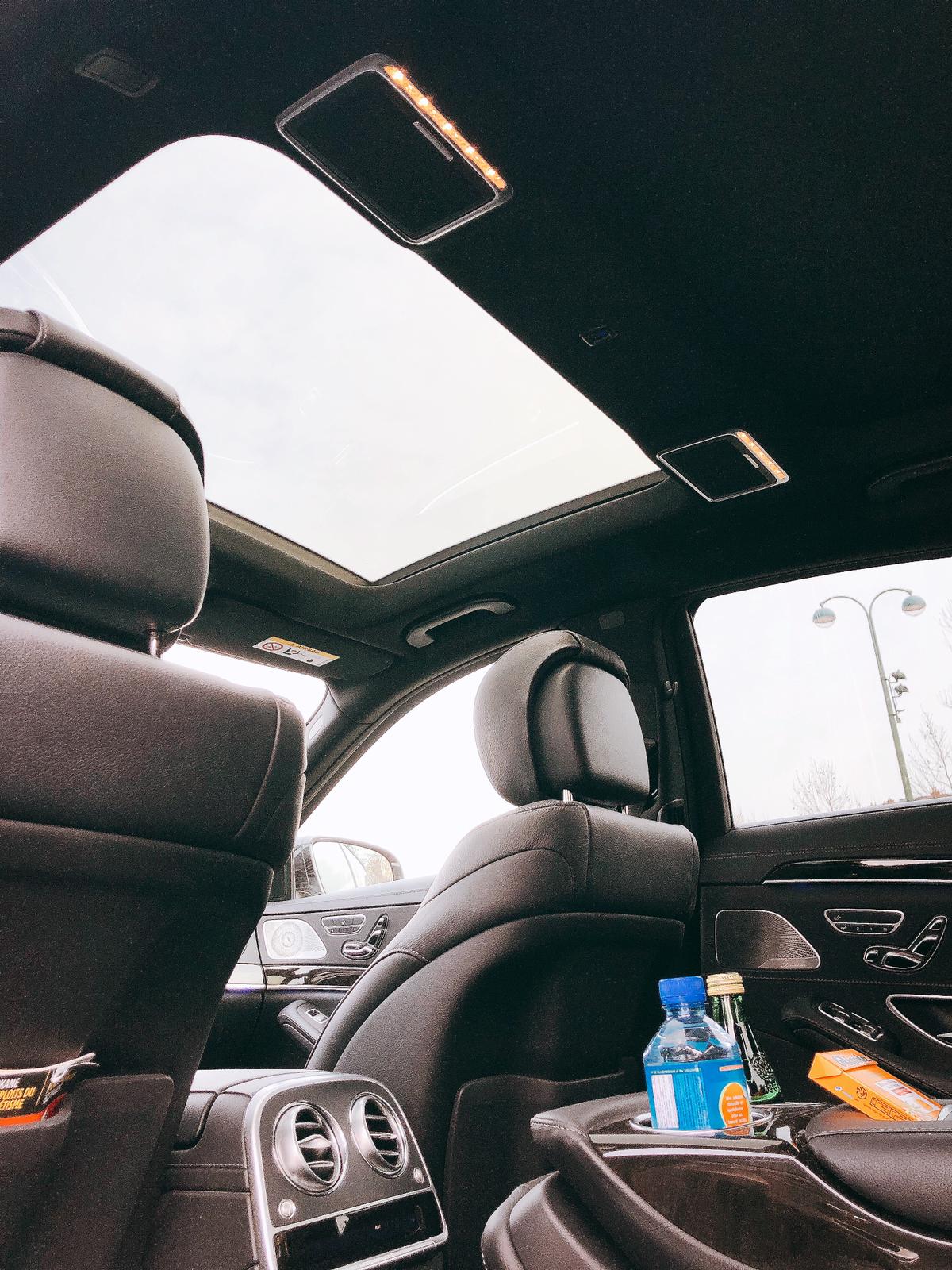 Intérieur de voiture de luxe avec sièges en cuir noir, toit ouvrant panoramique et porte-gobelets contenant des bouteilles et collations.
