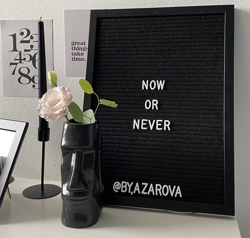 A vase with a flower and a painting with an inscription are on the table